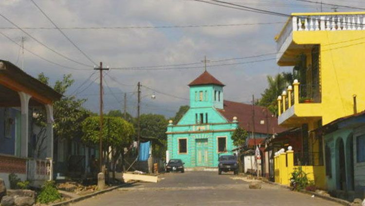 La imagen muestra una iglesia de color turquesa en una calle rural de Guatemala. Chocolá