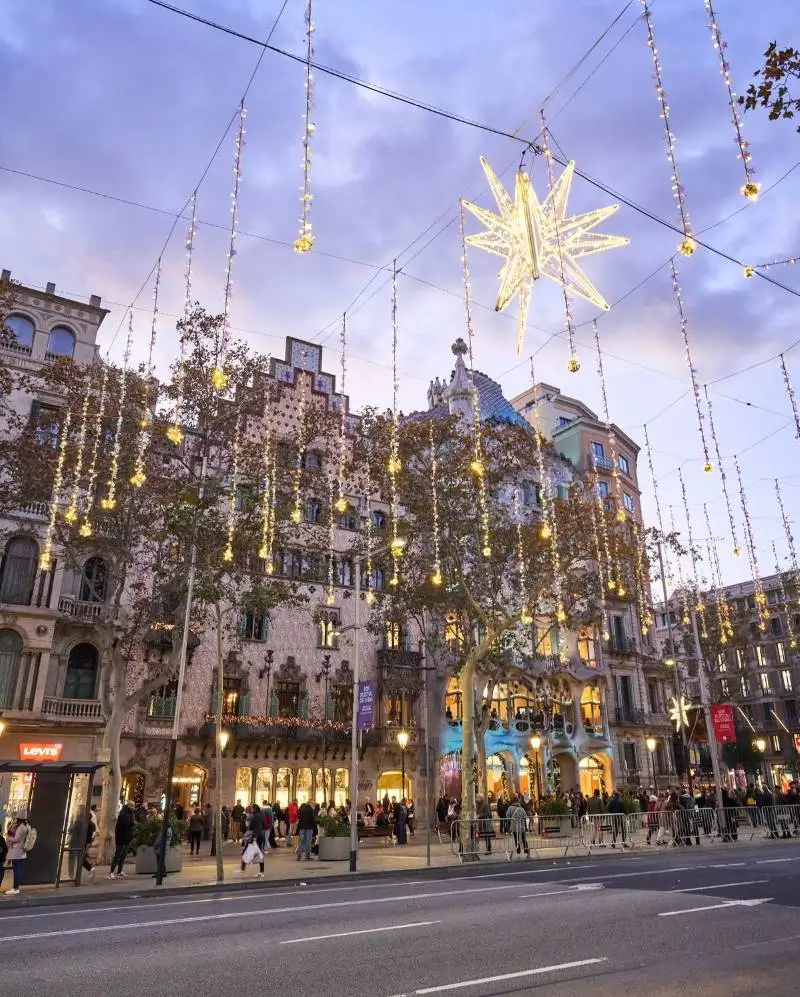 La imagen muestra la Casa Batlló en el Paseo de Gracia de Barcelona, iluminada con decoraciones navideñas. Esta obra maestra del modernismo catalán fue diseñada por Antoni Gaudí y es un icono de la ciudad. Volar en navidad a España