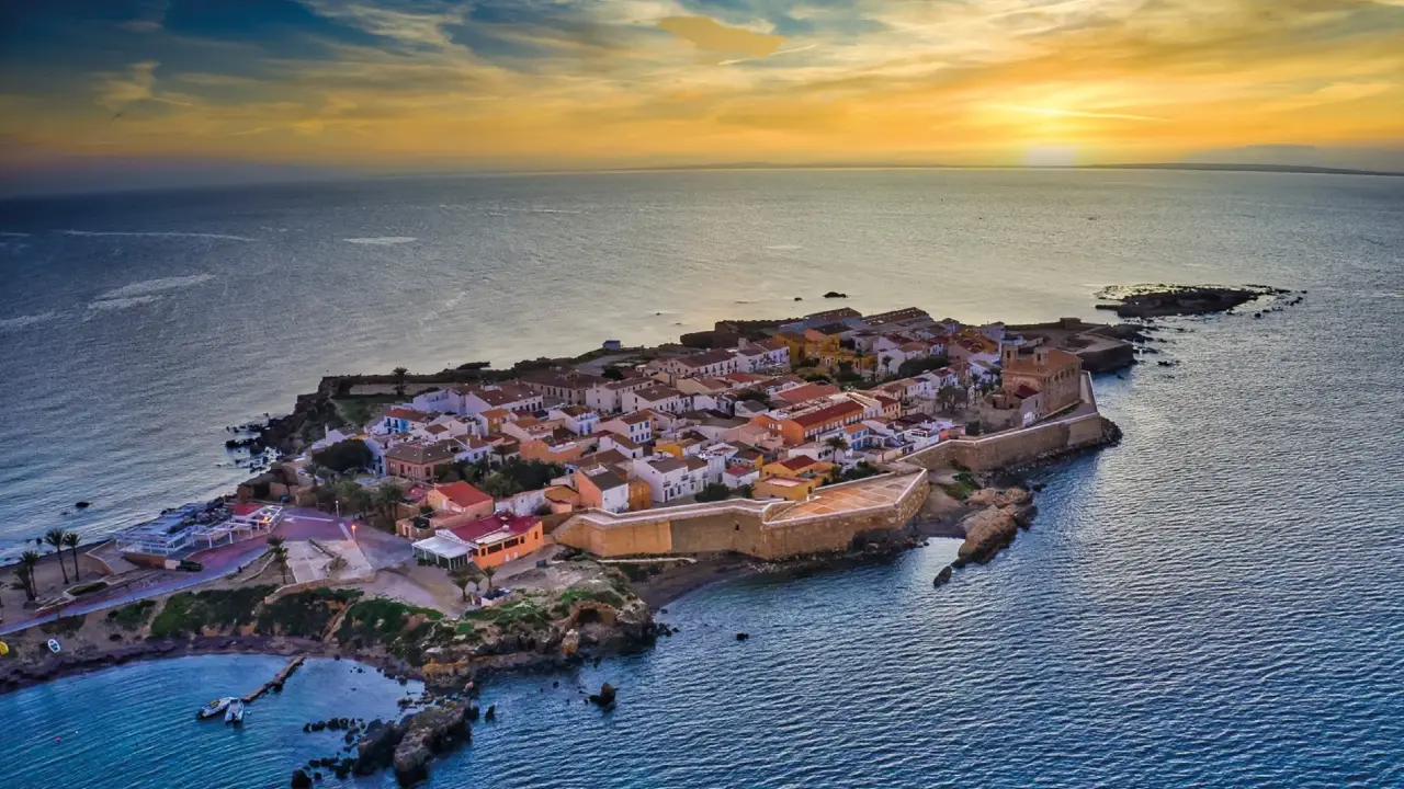 Vista aérea de la fortificada Isla de Tabarca al atardecer, con edificios de tonos cálidos y el mar Mediterráneo circundante.