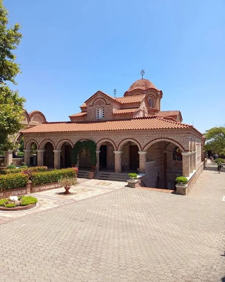 La imagen muestra el Monasterio de San Efraín el Sirio, un monasterio ortodoxo oriental. Se encuentra en Nea Makri, Grecia.El monasterio fue establecido en 1983.Es conocido por su arquitectura tradicional griega, con techos de tejas rojas y arcos de piedra.