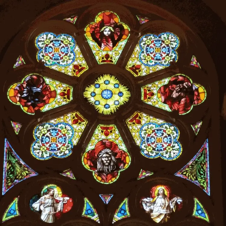 La imagen muestra un vitral eclesiástico de gran riqueza simbólica y cromática, perteneciente a ls Basílica de San Josafat en Milwaukee. Su diseño es simétrico y está centrado en un motivo circular con formas florales en tonos azules y amarillos, que evocan la luz divina o la creación.