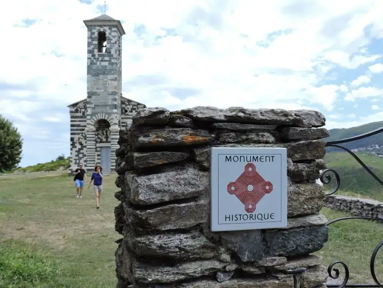 La imagen muestra a visitantes explorando la Iglesia de San Michele de Murato en Córcega, Francia, un destacado ejemplo de arquitectura románica del siglo XII. 