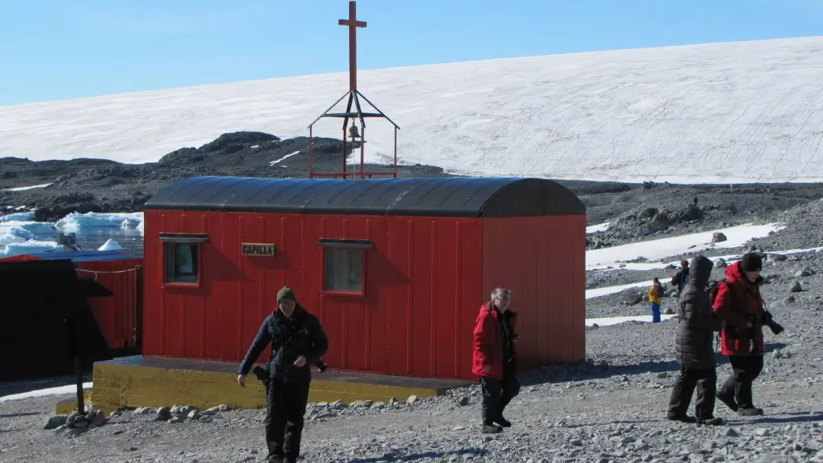Esta fotografía captura la capilla San Francisco de Asis una de las 7 capillas argentinas en la Antártida, un pequeño edificio rojo con una cruz en la cima, rodeado de nieve y hielo. Situada en la costa argentina, esta estación de investigación sirve como un centro científico clave para el estudio del entorno y el clima del continente.