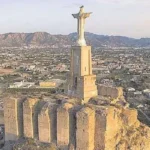Este es el Castillo de Monteagudo, una fortaleza de origen islámico del siglo XI situada en Murcia, España.La estatua en la cima es el Cristo de Monteagudo, una escultura de 14 metros de altura que replica la famosa estatua de Río de Janeiro.