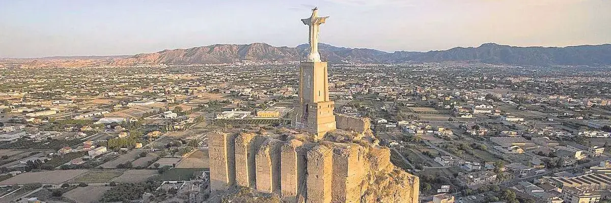 Este es el Castillo de Monteagudo, una fortaleza de origen islámico del siglo XI situada en Murcia, España.La estatua en la cima es el Cristo de Monteagudo, una escultura de 14 metros de altura que replica la famosa estatua de Río de Janeiro.
