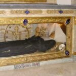 La imagen muestra el cuerpo atribuido como incorrupto de santa Catalina Labouré, el cual se encuentra reposando dentro de una urna de vidrio y bronce dorado en la Capilla de Nuestra Señora de la Medalla Milagrosa, ubicada en la Rue du Bac en París, Francia
