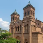 La imagen muestra la imponente Catedral Basílica Metropolitana de Medellín, ubicada frente al Parque Bolívar en Colombia. Este templo católico destaca por ser una de las construcciones en ladrillo macizo (adobe cocido) más grandes del mundo, diseñada en estilo neorrománico por el arquitecto francés Charles Émile Carré