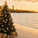 árbol de Navidad decorado con motivos marinos (como estrellas de mar) colocado en la arena de una playa tropical al atardecer, junto al mar.