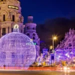 Esta fotografía muestra la Gran Vía de Madrid iluminada con un gran esfera navideña de luces y decoraciones brillantes en la noche. Durante la época festiva, la calle se transforma en un espectáculo de luces que atrae a millones de visitantes cada año.